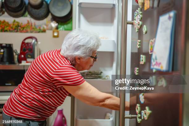 an elderly woman is taking something out of the refrigerator. - reusable food bag stock pictures, royalty-free photos & images
