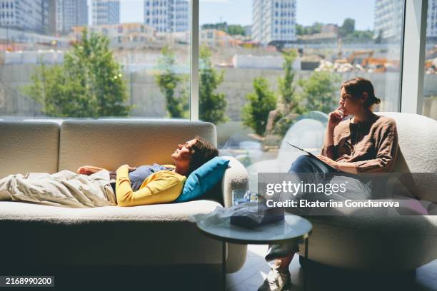 woman lying on a sofa in a therapy session. counselor sitting beside her with a clipboard. large windows showing cityscape. - psychiatrists couch stock pictures, royalty-free photos & images