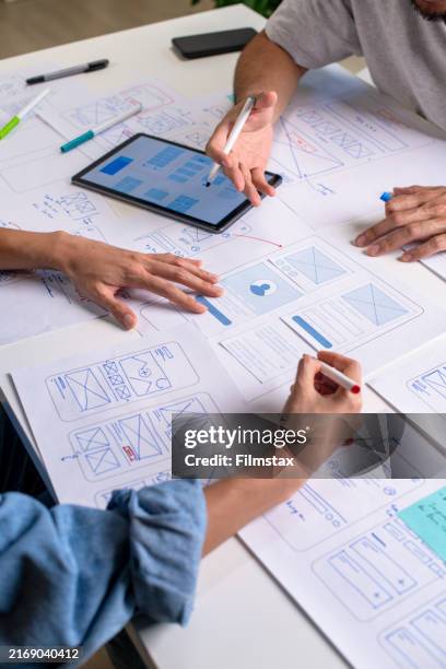 diseñadores de ux/ui discutiendo y haciendo una lluvia de ideas sobre wireframes para un sitio web y un prototipo de aplicación móvil, rodeados de bocetos del flujo de usuarios y herramientas de diseño, en el concepto de diseño de sitios web y aplicac - experiencia del usuario fotografías e imágenes de stock