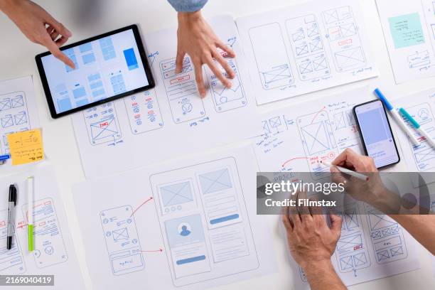 ux/ui designers discussing and brainstorming on wireframes for a website and mobile app prototype, surrounded by sketches of user flow and design tools, in the concept of website and mobile application design concept. - estilo imagens e fotografias de stock