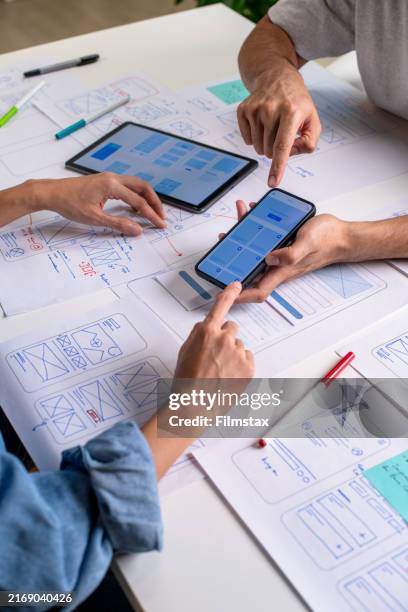ux/ui designer testing prototype on a phone, discussing and brainstorming on wireframes for a website and mobile app prototype, surrounded by sketches of user flow and design tools, in the concept of website and mobile application design concept. - ux elements stock pictures, royalty-free photos & images