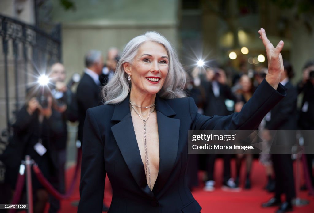 Woman with gray hair waving at red carpet event
