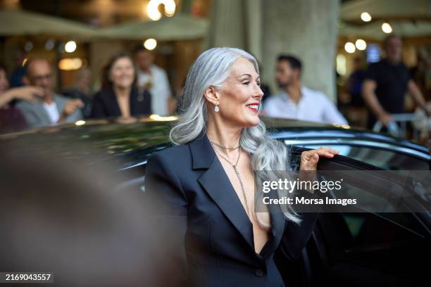 smiling woman stepping out from car at event - luxeauto stockfoto's en -beelden