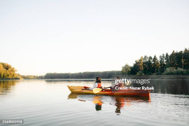 couple enjoying kayaking adventure on a serene lake at sunrise - kayak stock pictures, royalty-free photos & images