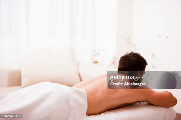 back view of a man lying on his stomach on a treatment bench - massage table stock pictures, royalty-free photos & images