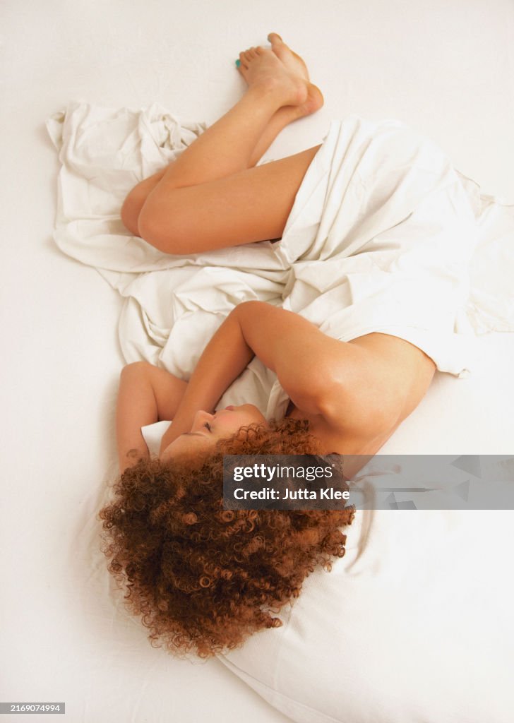 Woman Wrapped in Sheet Curled Up in Bed