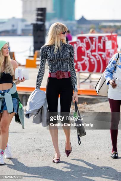 Guest wears long shirt, capri black pants, red belt during Oslo Fashion Week 2024 on August 28, 2024 in Oslo, Norway.