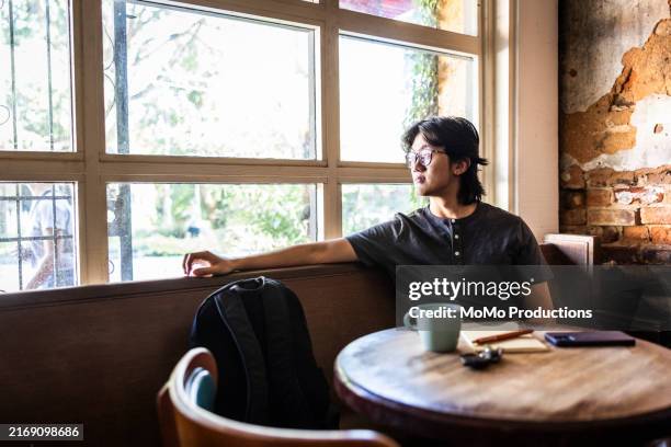 young man looking out window in cafe - view-through-restaurant-window stock pictures, royalty-free photos & images