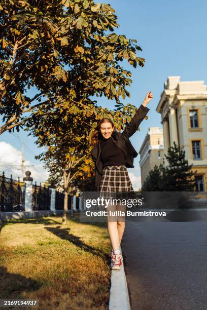 lively young woman strolls along college curb exuding happiness in academic journey ahead - jupe à carreaux photos et images de collection