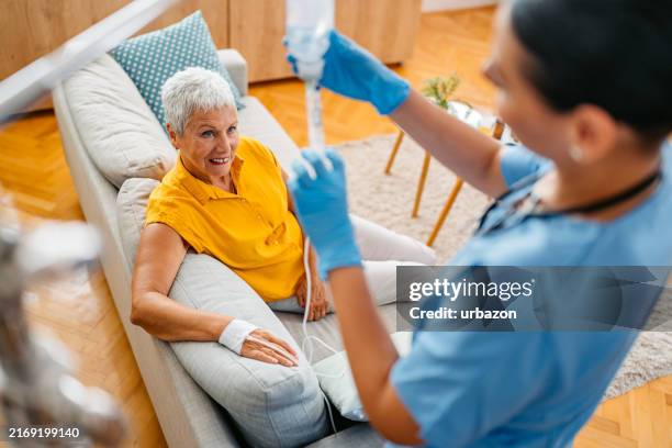 home care nurse adjusting iv drip on a senior woman while visiting her at her home - hemodialise imagens e fotografias de stock
