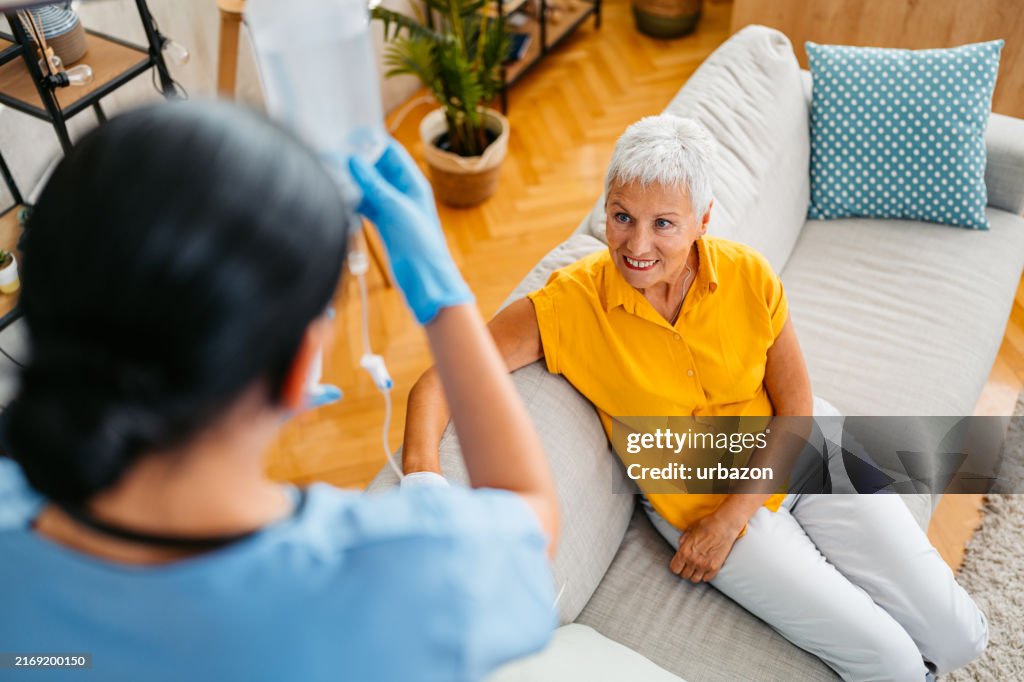 Home Care Nurse Adjusting IV Drip On A Senior Woman While Visiting Her At Her Home
