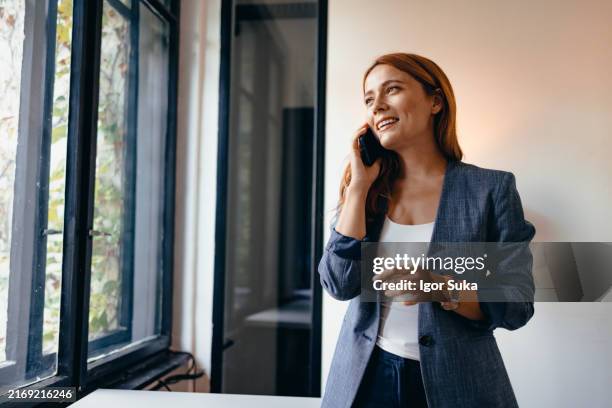 mujer de negocios hablando por teléfono en una oficina moderna con ventanas - casual chic fotografías e imágenes de stock