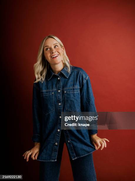 frau in jeansjacke und hose auf rotem hintergrund im studio - roter mantel stock-fotos und bilder