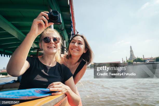 two caucasian women riding a boat on the chao phraya river while traveling in bangkok. - kulturen stock-fotos und bilder