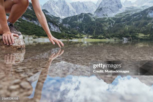 hand reaching down to touch lake surface - crouch water stock pictures, royalty-free photos & images
