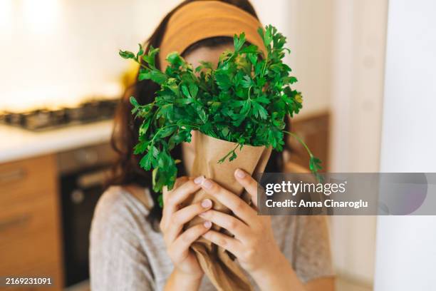 woman holding fresh parsley while cooking in a modern kitchen with wooden cabinets and a cozy atmosphere during the day - clorofila fotografías e imágenes de stock