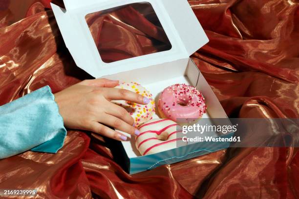 woman picking up donut from box over iridescent cloth - dónute imagens e fotografias de stock