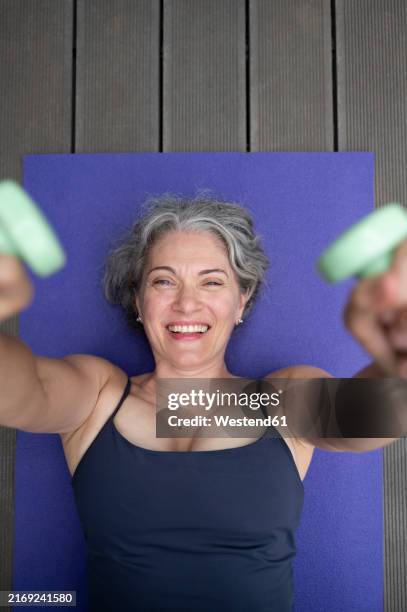 happy woman lying down and exercising with dumbbells on mat - hand weight stock pictures, royalty-free photos & images