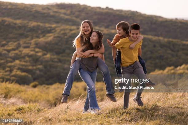 happy children playing piggy back on a mountain - sister stock pictures, royalty-free photos & images