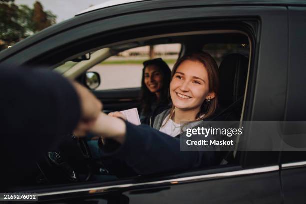 smiling young woman giving fist bump holding driving license while sitting in car - fahrschule stock-fotos und bilder