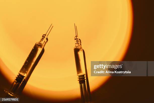 two syringes with needles against background of bright orange light, creates dramatic and intense effect - hormone stock pictures, royalty-free photos & images