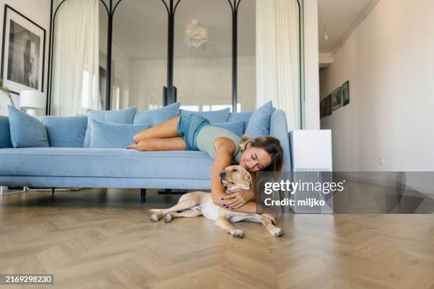 woman relaxing with her dog on sofa in her living room - air purifier stock pictures, royalty-free photos & images