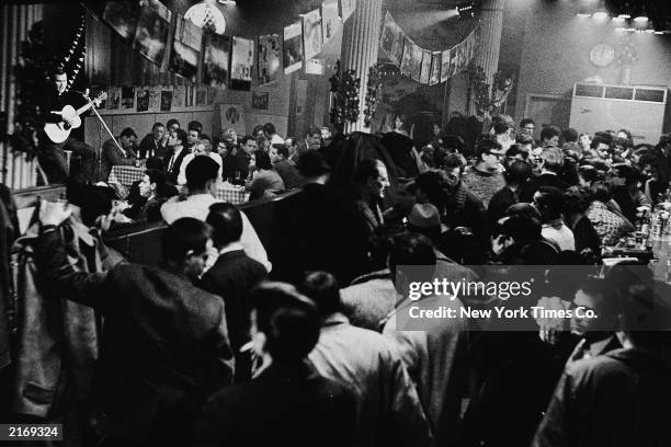 Folk musician plays acoustic guitar for a crowded audience inside Gerde's Folk City nightclub near West 4th Street and Broadway, Greenwich Village,...