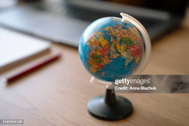 small world globe on the top of wooden desk. work environment of laptop and note pads in background. - jordglob bildbanksfoton och bilder
