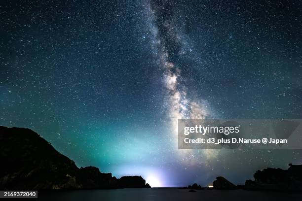 beautiful starry sky seen from nakagi port.the milky way in the center and a small mountain on the cape with togaihama beach on the right.in the foreground are the lights of the harbor breakwater and boats. - mitternacht stock-fotos und bilder