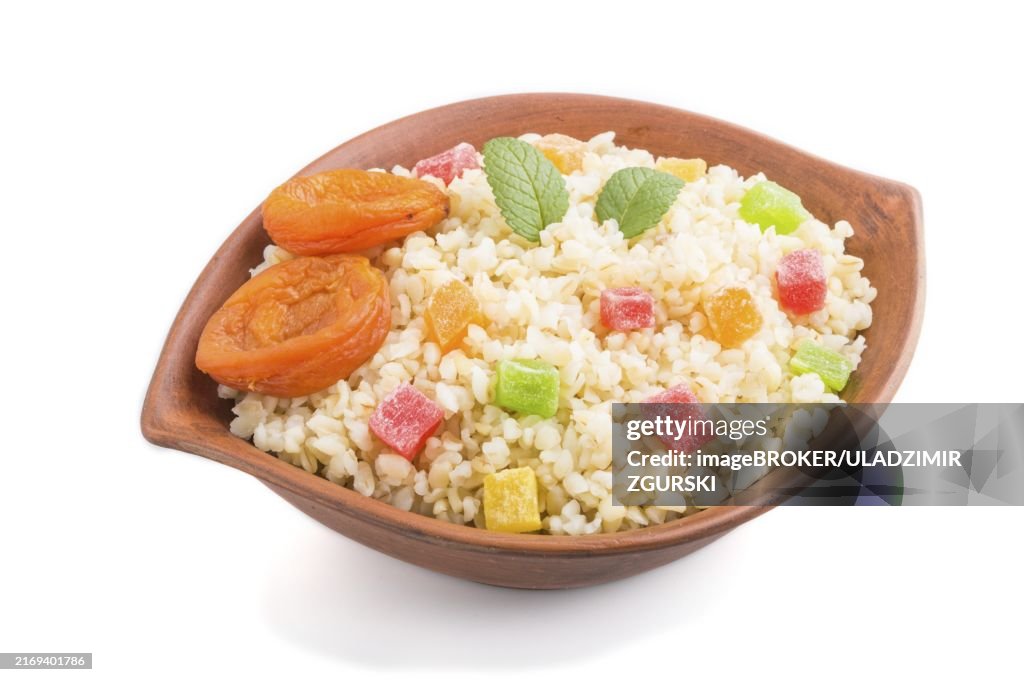 Bulgur porridge with dried apricots and candied fruits in clay bowl isolated on white background. Side view, close up. Turkish traditional cuisine