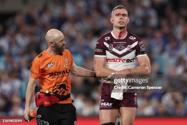 Tom Trbojevic of the Sea Eagles is assisted by a trainer after an injury and a head cut during the round 26 NRL match between Canterbury Bulldogs and...