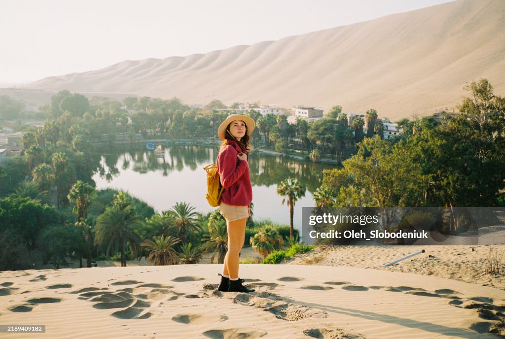 Woman standing on sand dune looking at oasis in Huacachina, shot on camera film