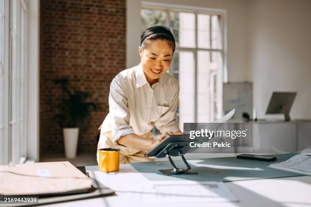 casually clothed female architect using digital tablet while working at modern office - modelo ocupação imagens e fotografias de stock