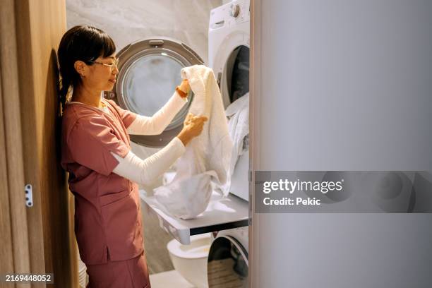 female nurse taking clothes out of washing machine at home - dirty uniform laundry stock pictures, royalty-free photos & images