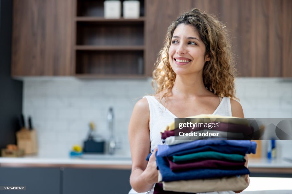 Happy woman holding a pile of clothes after finishing the laundry
