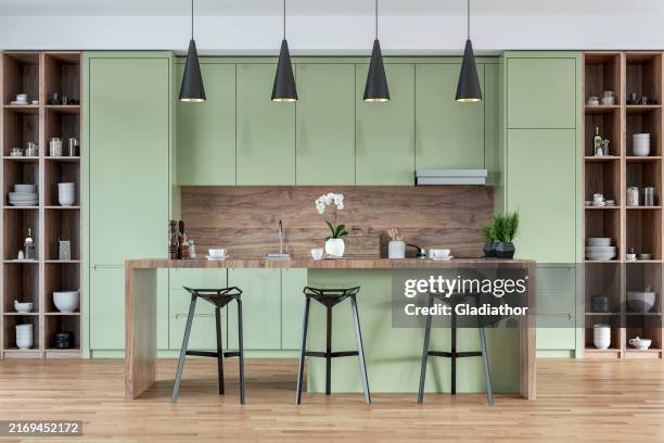 a front view of a modern pastel green, white and hardwood kitchen with rectangular breakfast kitchen island with stools, pendant lights - kitchen front view stock pictures, royalty-free photos & images