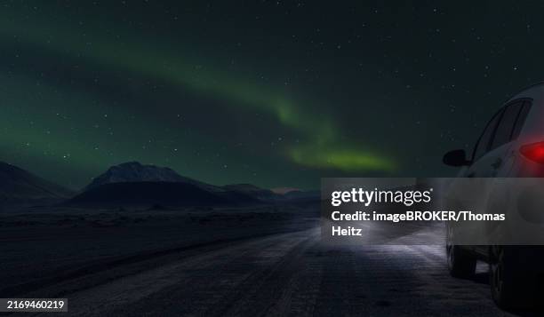 a car with its lights on, standing on a country road in iceland, with aurora borealis in the background - iceland northern lights stock illustrations