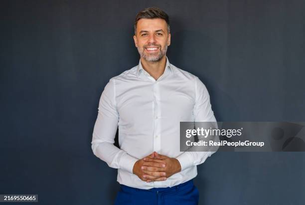 lächelnder mann, der in weißem hemd vor dunklem hintergrund posiert - weißes hemd stock-fotos und bilder