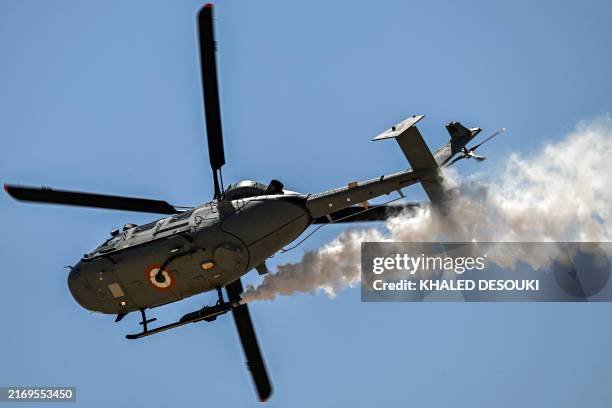 An Indian Air Force HAL Dhruv utility helicopter releases smoke while performing manoeuvres during the first Egypt International Airshow at Alamein...