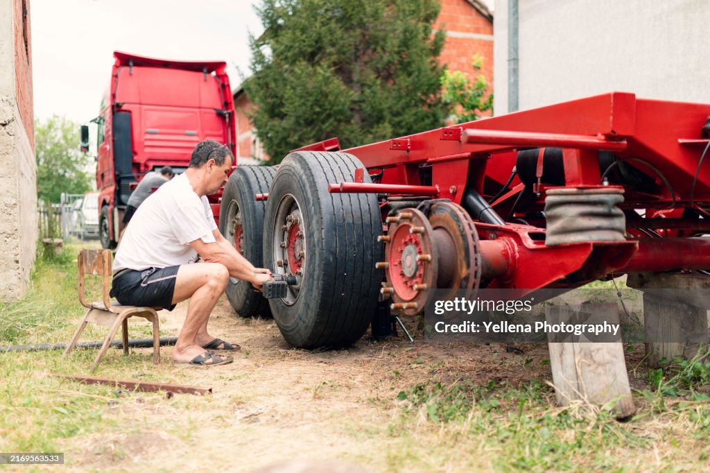 The man is using a screw gun on a trailer wheel bolts.