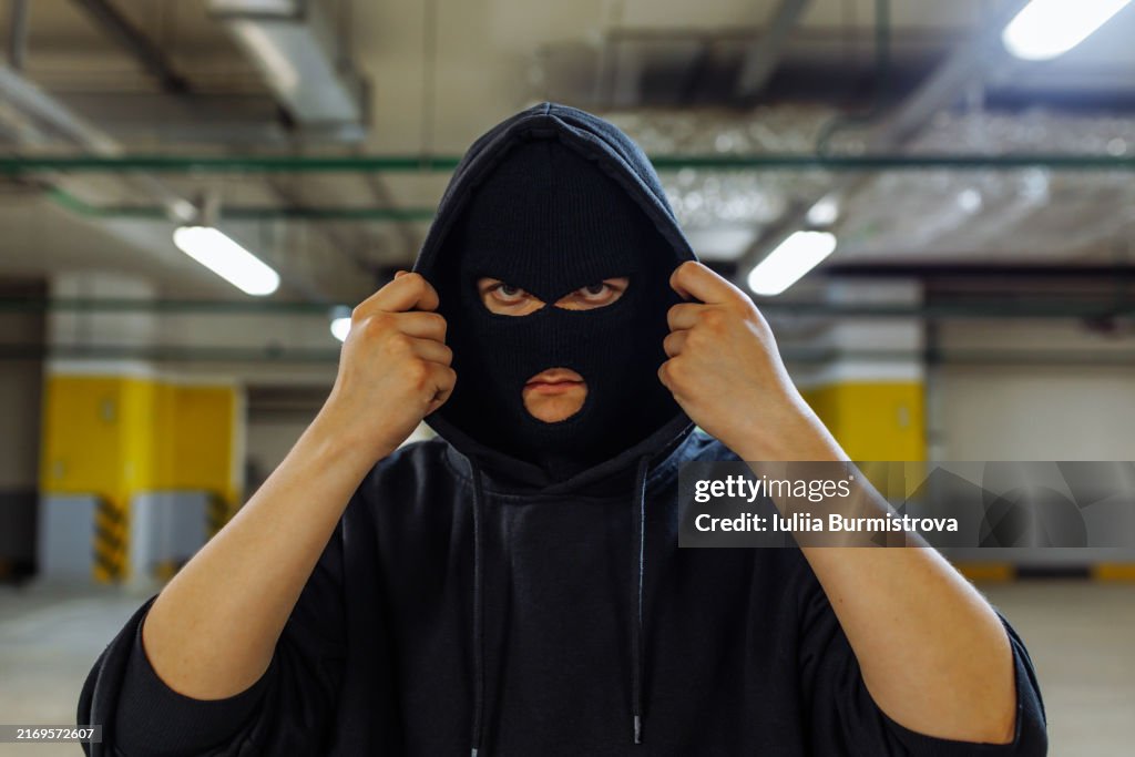 Sinister-looking young man wearing face mask and hooded sweatshirt standing in empty parking garage