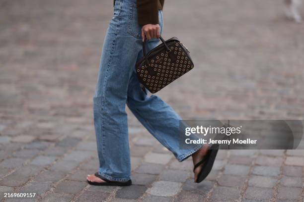 Fashion Week guest is seen wearing a brown cardigan, light blue jeans with straight leg, a rectangular dark brown leather bag with golden eyelets...