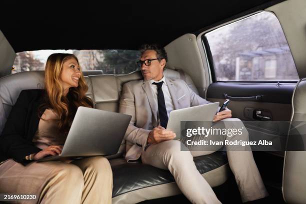 business people working on laptops and using technology in backseat of limousine - limousine stock pictures, royalty-free photos & images