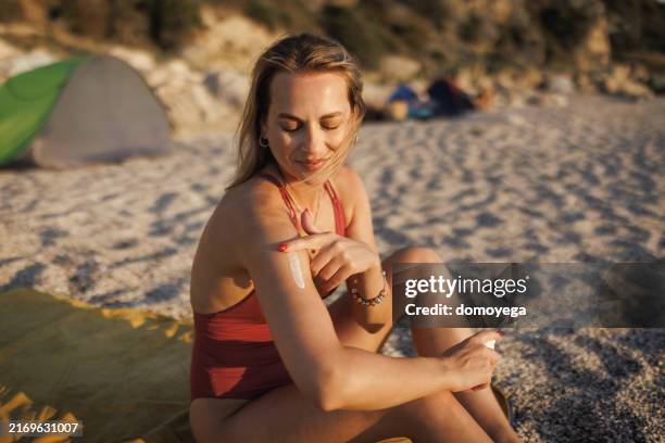 young woman applying sunscreen at the beach - badkläder bildbanksfoton och bilder