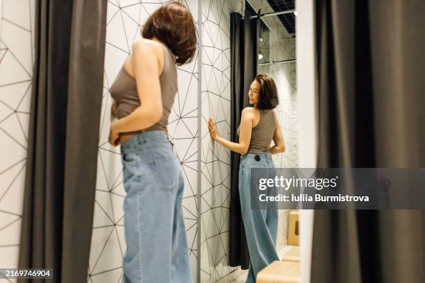 attractive woman checking out how her buttocks look in denim jeans in fitting room - bob haircut hairstyle back stock pictures, royalty-free photos & images