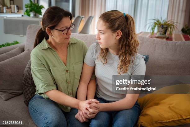 mother and daughter sitting on sofa holding hands and talking about adolescence problems - support bildbanksfoton och bilder