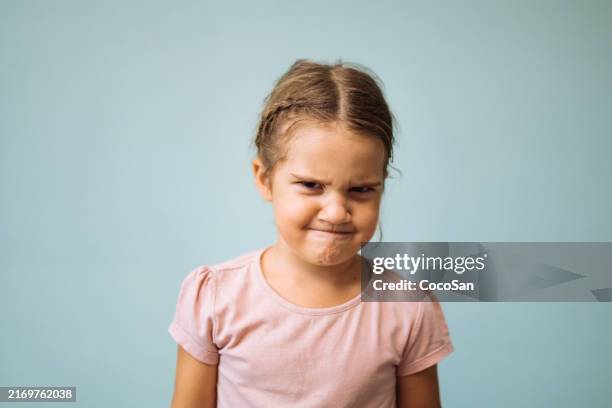 jovem expressando descontentamento com uma carranca no rosto, de pé contra um fundo azul claro enquanto usava uma camisa rosa. - franzindo as sobrancelhas - fotografias e filmes do acervo