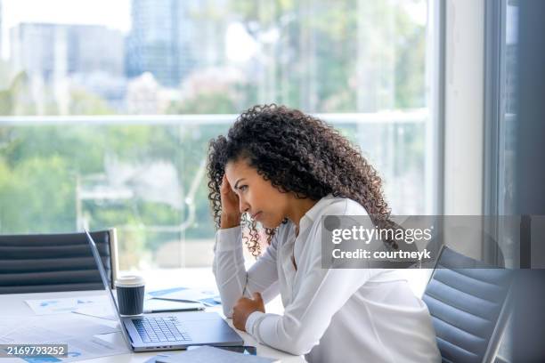 donna sconvolta che lavora su un computer portatile in ufficio. sembra preoccupata, frustrata e depressa - lentezza foto e immagini stock