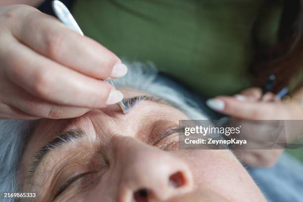 a beautician is plucking an elderly woman's eyebrows with tweezers. - tweezing eyebrows stock pictures, royalty-free photos & images