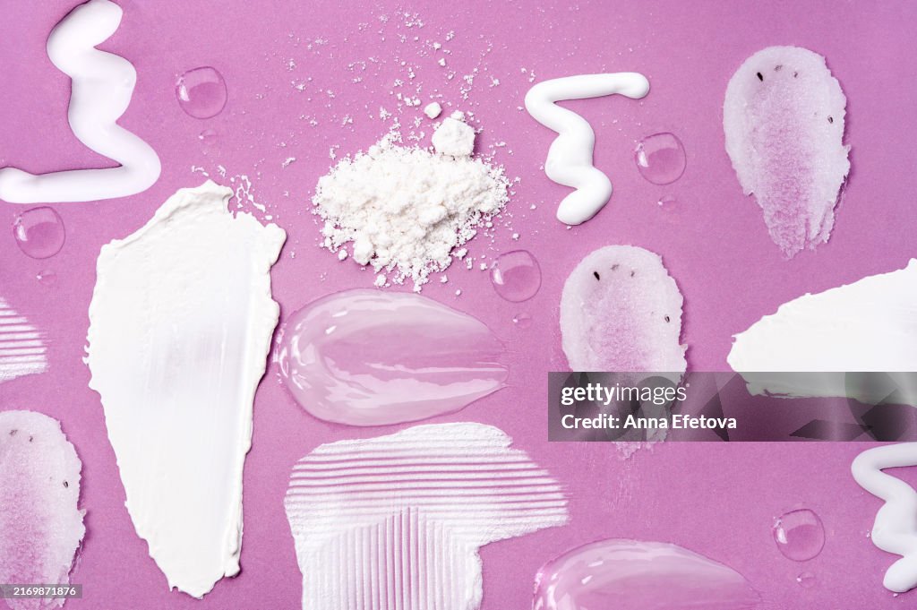 Various textures of cosmetic creams, lotions, serums, and exfoliants spread across a purple background. Includes creamy moisturizers, translucent gel serums, exfoliating scrubs with particles, and fine cosmetic powders. Ideal for highlighting skincare pro